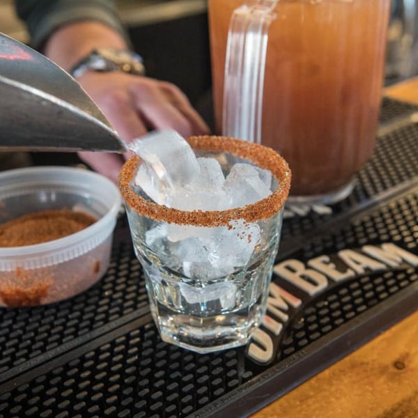 Bartender pouring ice into a spice-rimmed glass, with a pitcher of Yazoo BBQ's signature drink nearby.