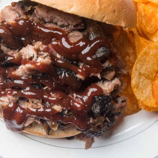 Close-up of a Yazoo BBQ pulled pork sandwich with barbecue sauce and a side of chips.