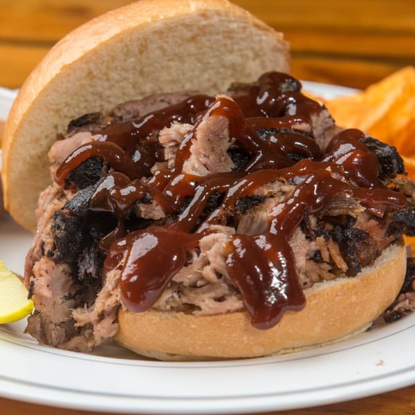 Close-up of a Yazoo BBQ pulled pork sandwich with dark barbecue sauce, served with chips.