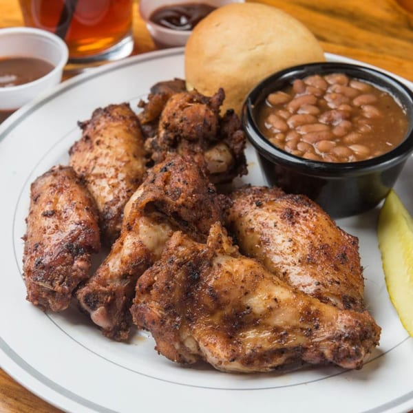 Yazoo BBQ chicken wings, baked beans, and a roll on a white plate with a pickle spear.