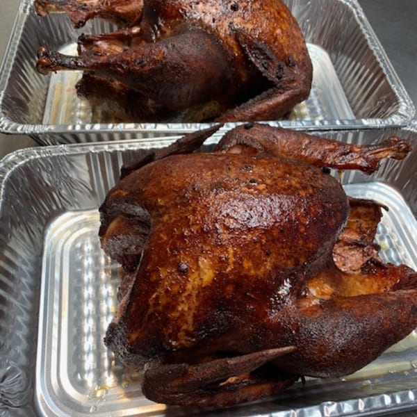 Two whole smoked turkeys with crispy, dark brown skin in aluminum foil pans.