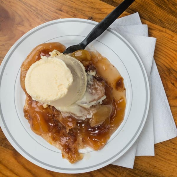 Yazoo BBQ's peach cobbler with a scoop of vanilla ice cream on a white plate.