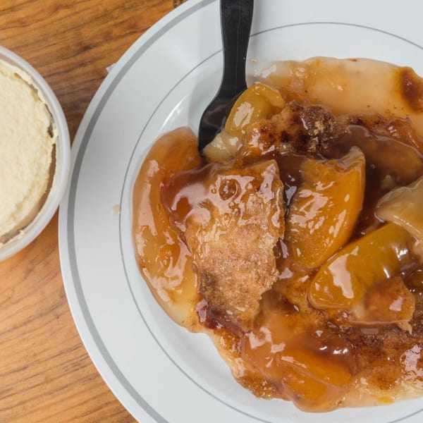 Close-up of Yazoo BBQ's peach cobbler with a black spoon and a side of whipped cream.