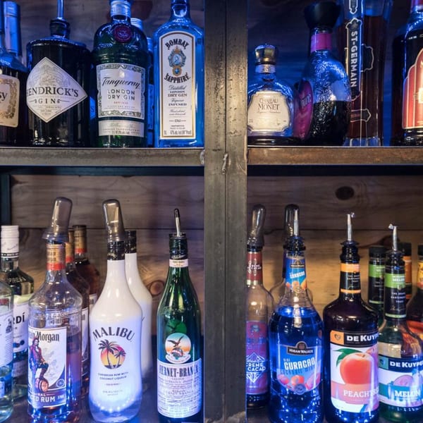 Liquor bottles, including gin, rum, and liqueurs, neatly arranged on wooden shelves in a bar.