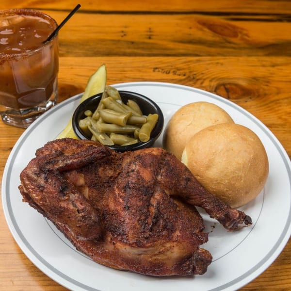 A plate of Yazoo BBQ chicken, green beans, rolls, and a drink on a wooden table.