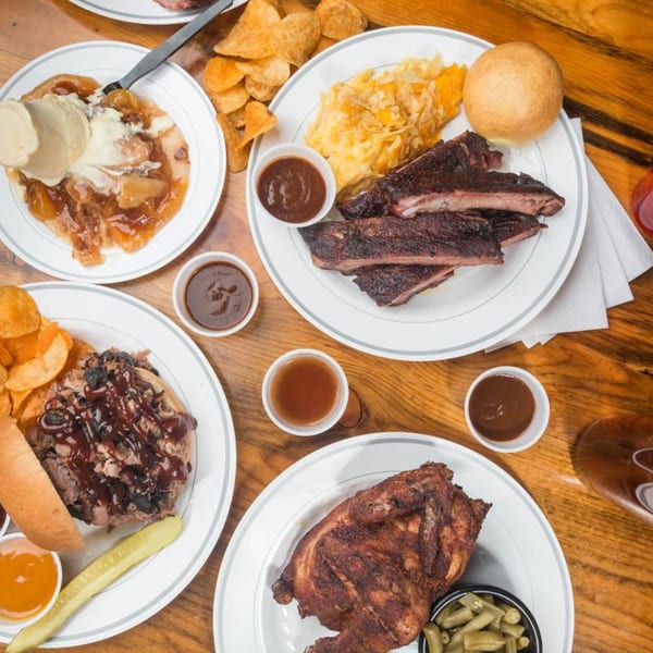 Overhead view of a wooden table laden with various Yazoo BBQ dishes, including ribs, chicken, and dessert.
