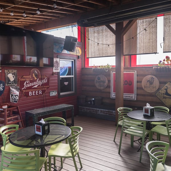 Outdoor patio at Yazoo BBQ with green chairs, black tables, and beer signs on red and wood walls.