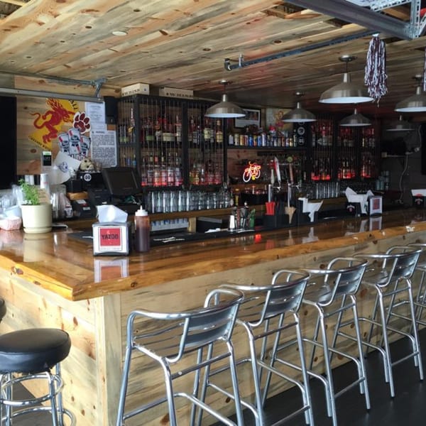 The Yazoo BBQ bar features a wooden counter with metal stools and a fully stocked liquor shelf.