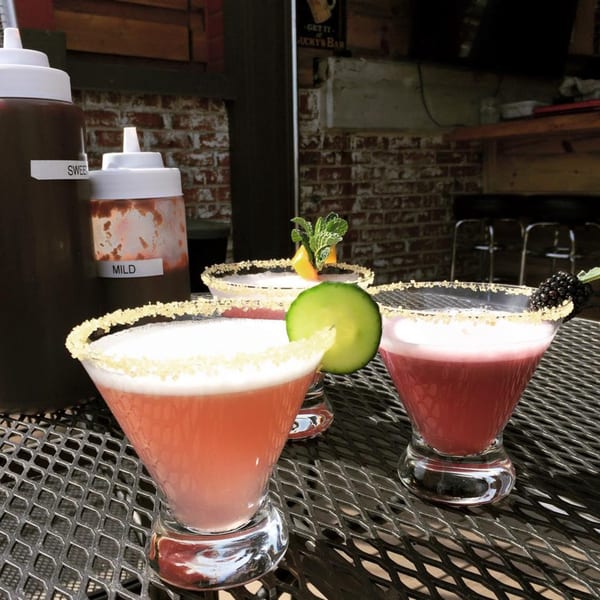 Three colorful cocktails with sugared rims and garnishes on a metal table at Yazoo BBQ.